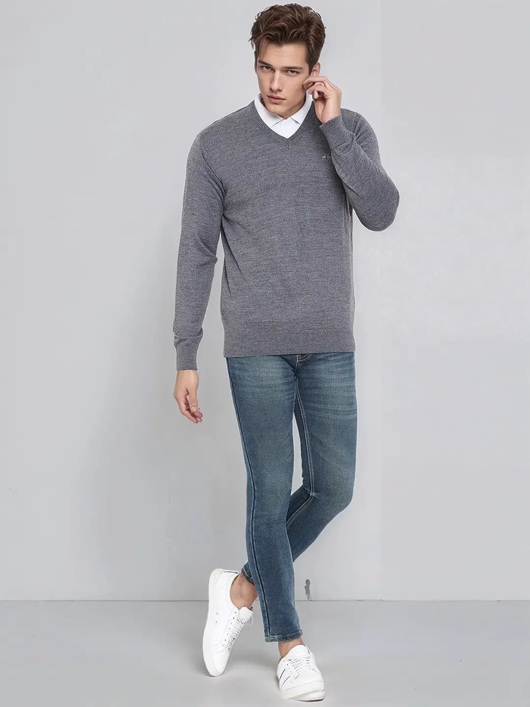 Man in 98degreenorth Men’s Medium Grey Merino Wool V-Neck Sweater, white shirt, blue jeans, stands casually.