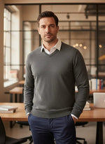 A man wears the 98degreenorth Men’s Medium Grey Merino Wool V-Neck Sweater in a modern office with glass walls.