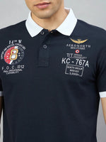 Man wears Men's Navy Aeronorth KC-767A Aviation Polo T-Shirt by 98degreenorth with white collar and embroidered patches.