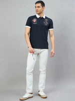 Man in a Men's Navy Aeronorth KC-767A Aviation Polo T-Shirt by 98degreenorth, white jeans, holding sunglasses.