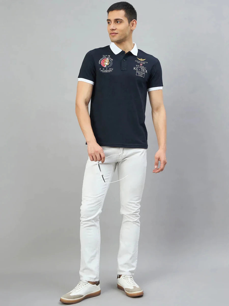 Man in a Men's Navy Aeronorth KC-767A Aviation Polo T-Shirt by 98degreenorth, white jeans, holding sunglasses.