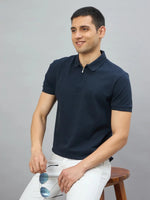 Man in a 98degreenorth Navy Blue Quarter Zip Polo T-Shirt smiles on a stool, holding sunglasses.