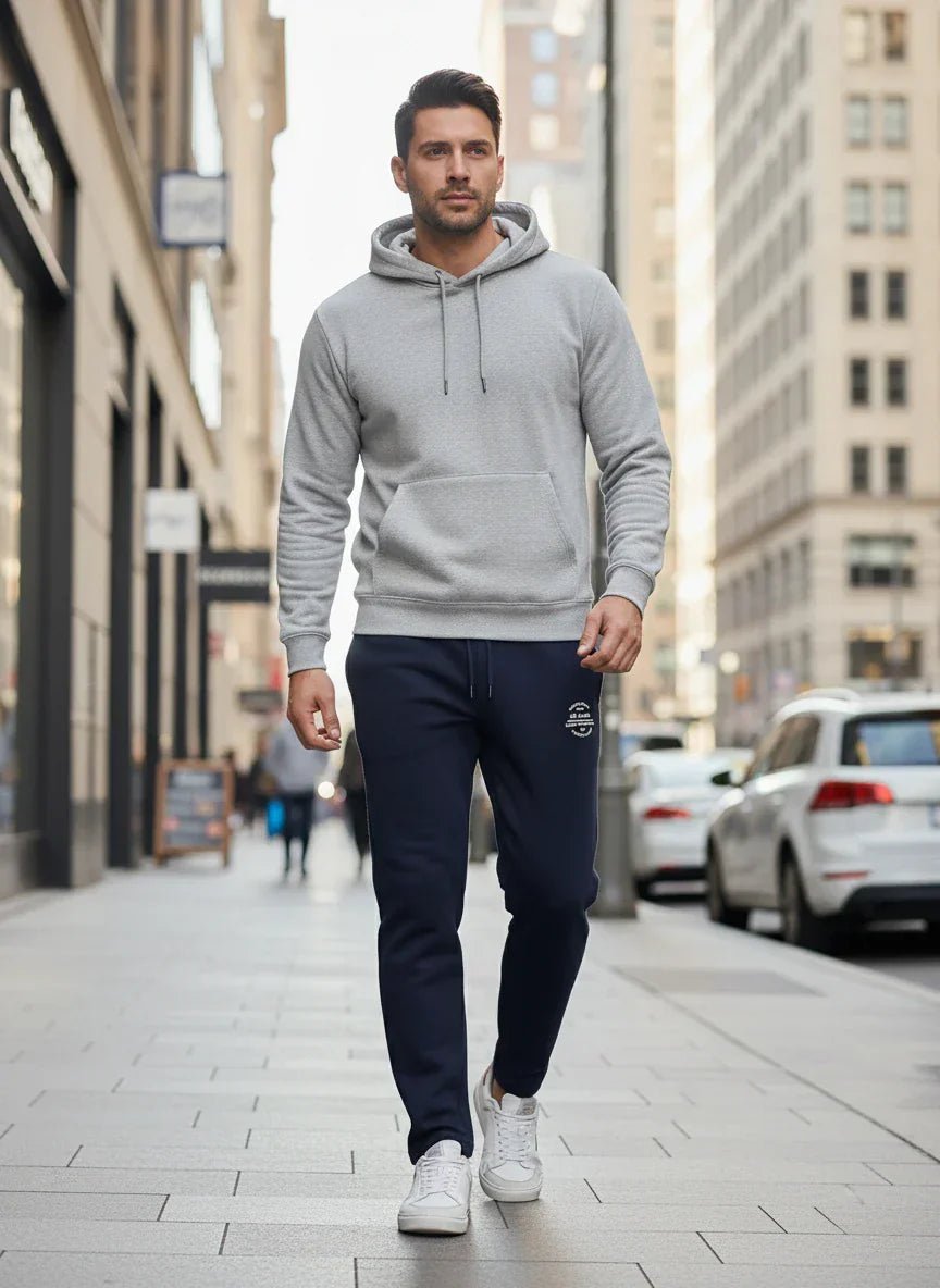A man wears 98degreenorth Men’s Navy Fleece Trackpants – Classic Warm Joggers while walking on a city sidewalk.