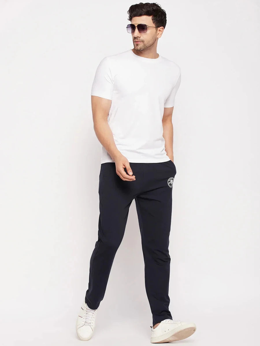 Man in 98degreenorth Navy French Terry Lycra Trackpants, white tee, sunglasses & sneakers against plain background.