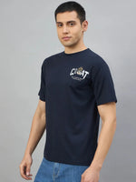 Man wearing 98degreenorth Men's Navy Graphic Oversized T-Shirt with GOAT back print, against a grey background.