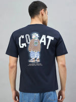 A man in a 98degreenorth navy oversized T-shirt with GOAT back graphic stands against a plain background.