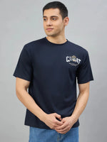 Man in a 98degreenorth Men's Navy Graphic Oversized T-Shirt and blue jeans, standing against a gray background.