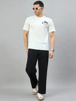Man in white sunglasses, 98degreenorth Men's Off-White Graphic Oversized T-Shirt, black pants & white sneakers by gray background.