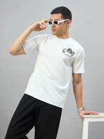 Man in 98degreenorth Men's Off-White Graphic Oversized T-Shirt poses, adjusting sunglasses on a white surface.