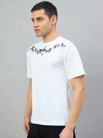 Man wears 98degreenorth Men's Off-White Graphic Oversized T-Shirt with chest text, against a plain grey background.