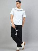 Man in a 98degreenorth Men's Off-White Graphic Oversized T-Shirt—They Made Me Do It Back Print, black pants, and sneakers.