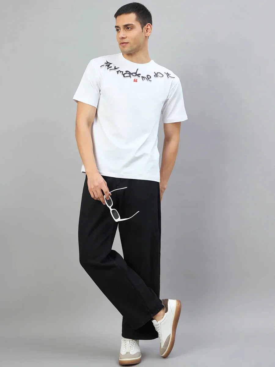 Man in a 98degreenorth Men's Off-White Graphic Oversized T-Shirt—They Made Me Do It Back Print, black pants, and sneakers.