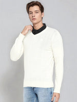A man wears the 98degreenorth Men’s Off-White Merino Wool V-Neck Sweater over a black shirt and blue jeans.