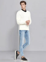 A man wears the 98degreenorth Men’s Off-White Merino Wool V-Neck Sweater and light blue jeans against a gray background.