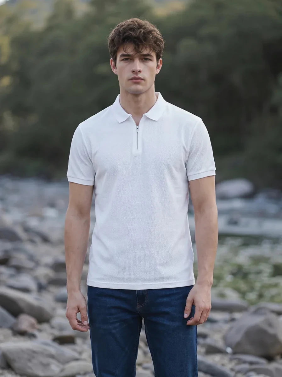 A man in a 98degreenorth off-white popcorn knit quarter zip polo and blue jeans stands outdoors on a rocky path.