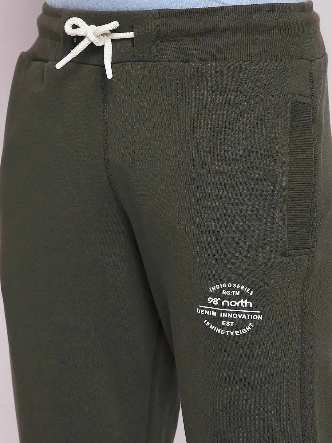 Close-up of 98degreenorth Men’s Olive Fleece Trackpants with white drawstring and printed text by the left pocket.
