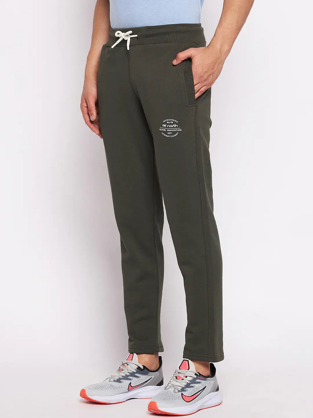 A person in 98degreenorth Men’s Olive Fleece Trackpants and a light blue shirt stands against a white background.