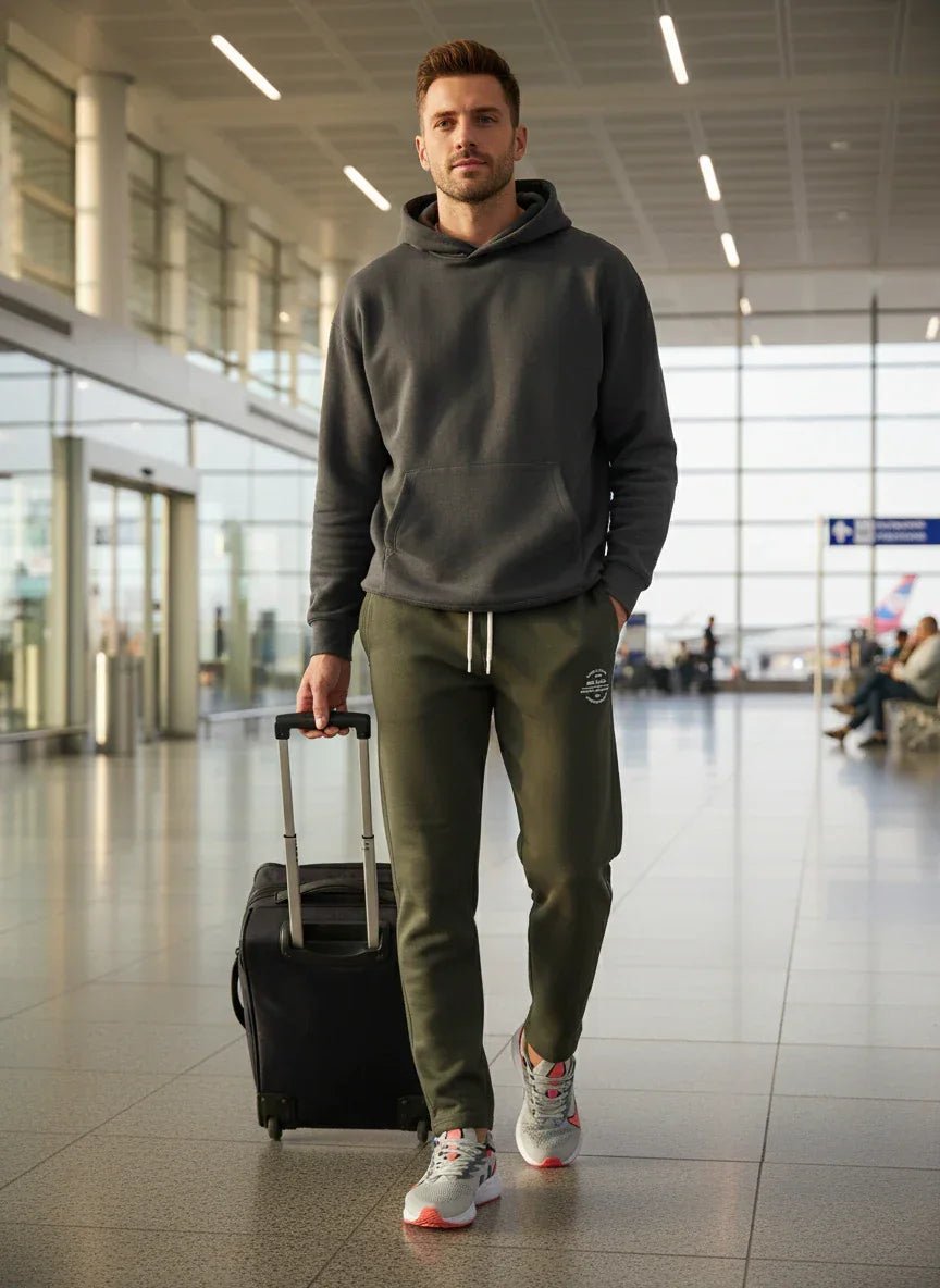 A man in 98degreenorth Men’s Olive Fleece Trackpants strolls through the airport with a suitcase, looking ahead.