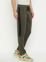 Man sports 98degreenorth Men’s Olive Fleece Trackpants, cream tee, and beige sneakers with green accents.