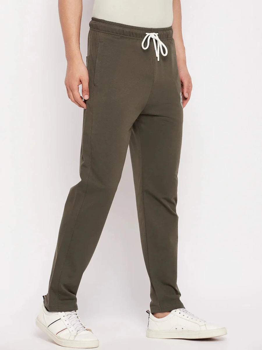 A man wears 98degreenorth Men's Olive French Terry Lycra Trackpants with white sneakers, standing against a white backdrop.