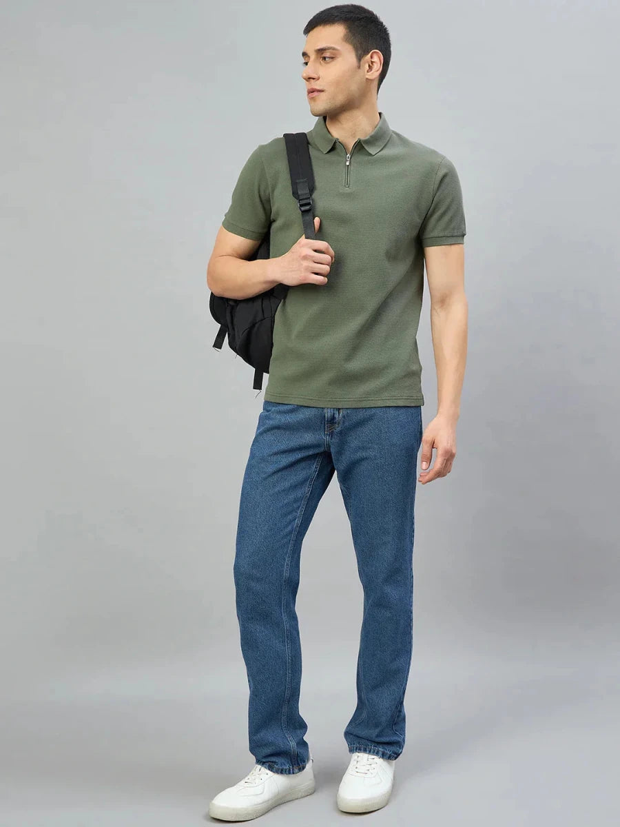 Man in 98° North Olive Green Quarter Zip Polo, blue jeans, white sneakers, with a black backpack on one shoulder.