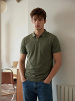 A man wears the 98degreenorth Men's Olive Green Quarter Zip Polo T-Shirt, standing indoors with hands in his pockets.