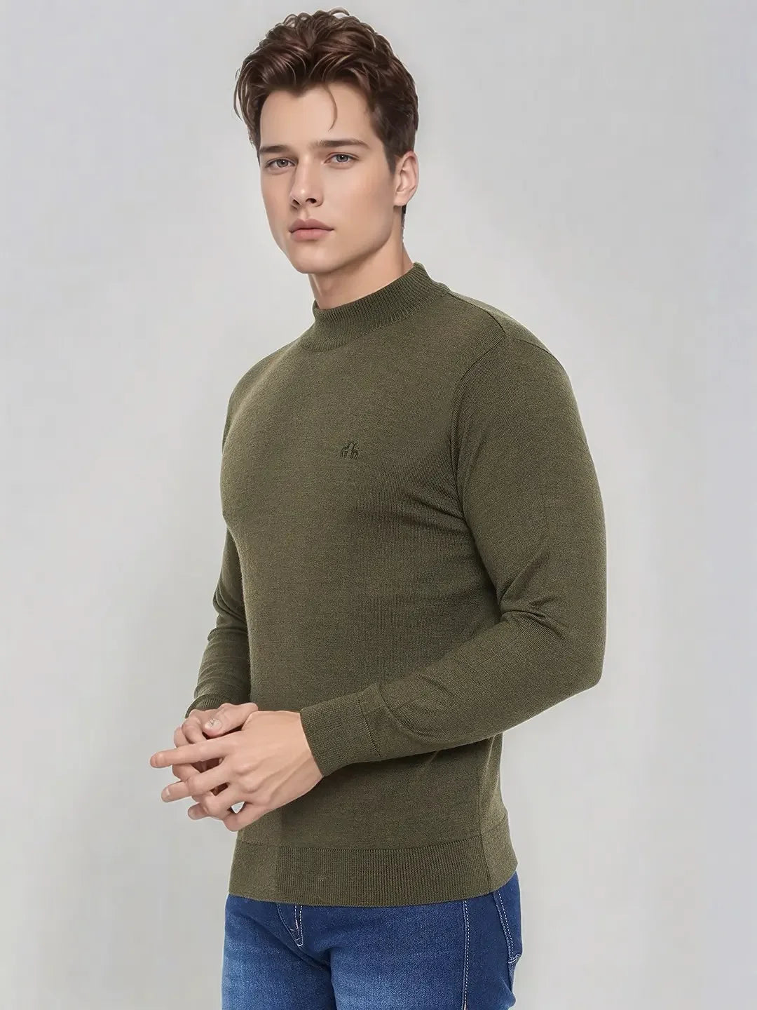 A man in a 98degreenorth Olive Merino Wool Turtle Neck Sweater and blue jeans stands against a light grey background.