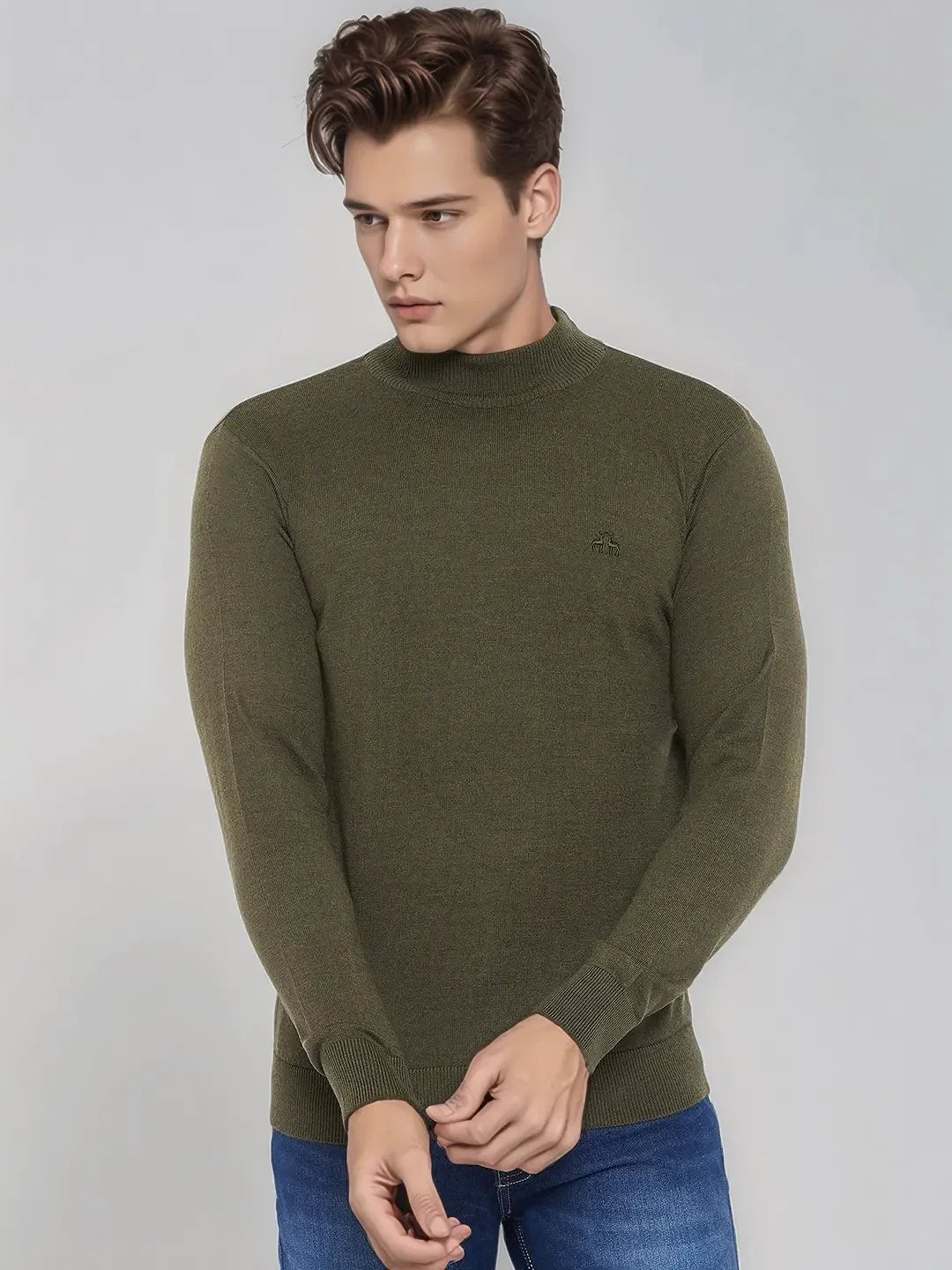 A man wears a 98degreenorth Men’s Olive Merino Wool Turtle Neck Sweater and blue jeans, standing against a light gray background.