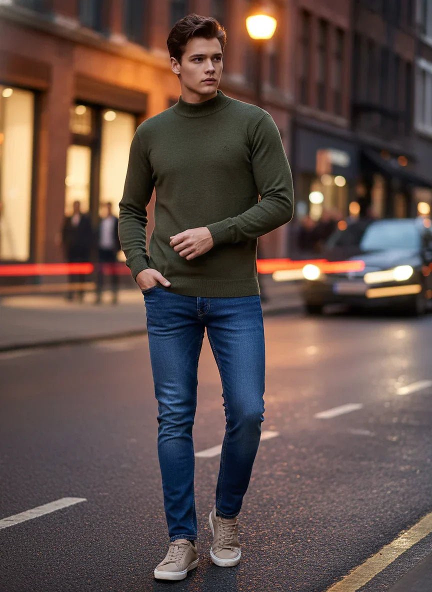 A man wears a 98degreenorth Men’s Olive Merino Wool Turtle Neck Sweater while walking on a city street at dusk.