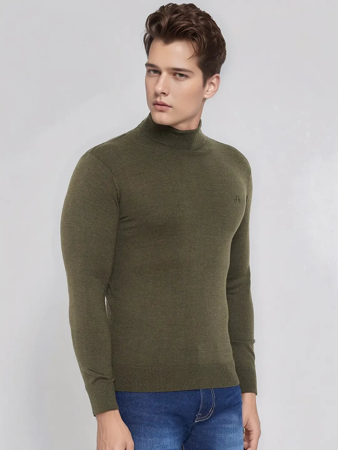 A man wears the 98degreenorth Men’s Olive Merino Wool Turtle Neck Sweater with blue jeans against a light gray background.