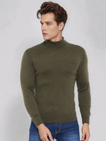 A man in a 98degreenorth olive merino wool turtle neck sweater and blue jeans stands against a light gray background.