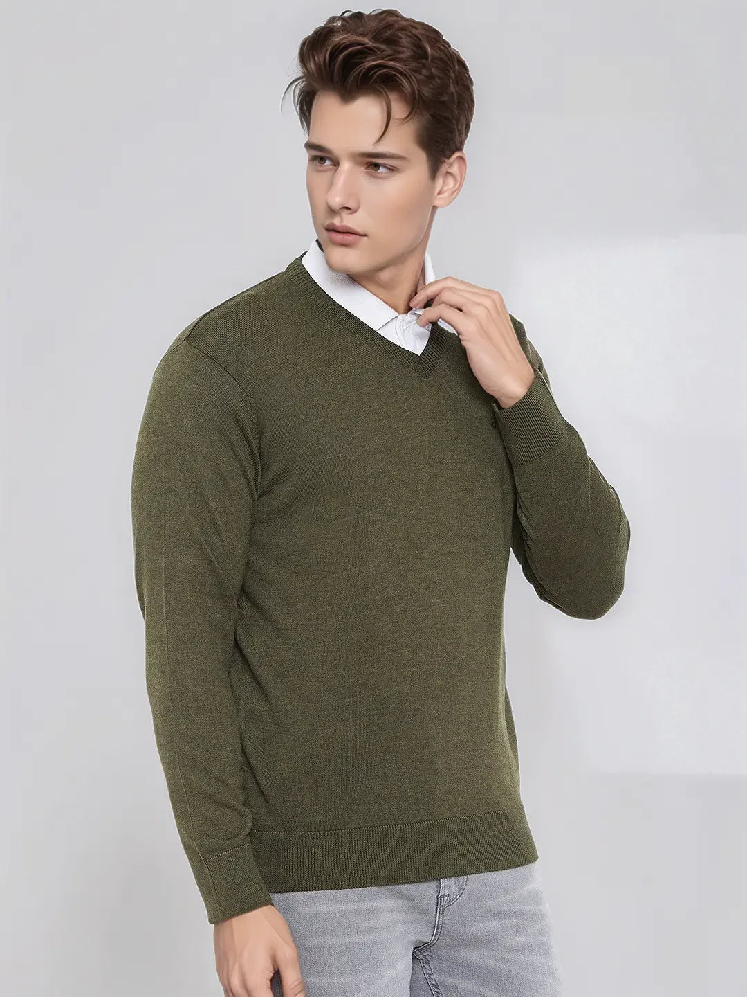 A young man in a Men’s Olive Merino Wool V-Neck Sweater by 98degreenorth poses against a light grey background.