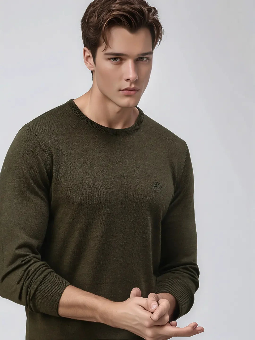 A young man in a 98degreenorth Men’s Olive Premium Merino Wool Round Neck Sweater poses against a grey background.