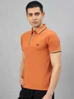 Man wears 98degreenorth Men's Orange Polo T-Shirt — Handmade Series with black pants against a gray background.