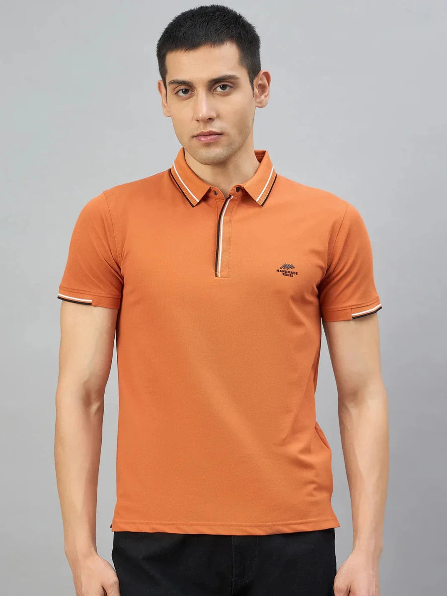 A man wears a 98degreenorth Men's Orange Polo T-Shirt—Handmade Series with contrast tipping and black trousers.