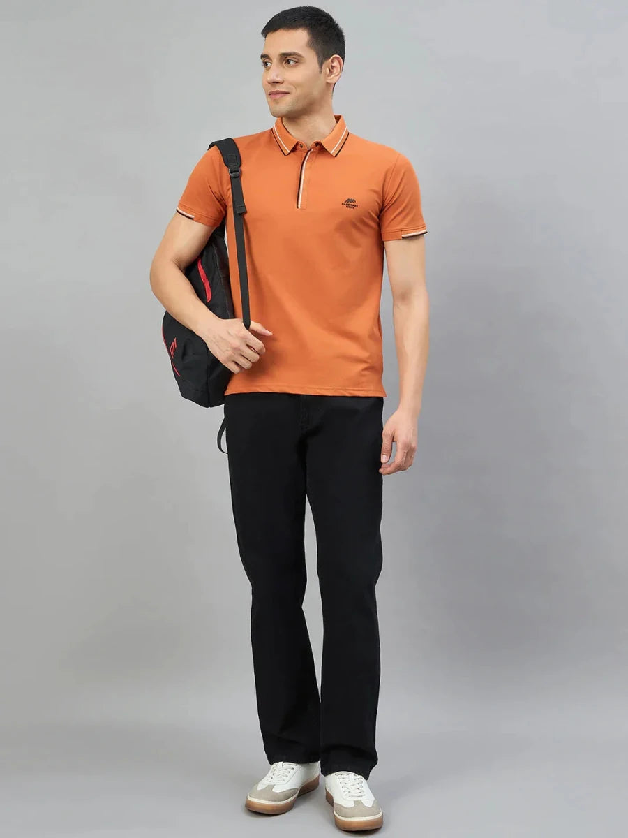 Man in 98degreenorth Men's Orange Polo T-Shirt—Handmade Series, black pants, white sneakers, and a black backpack.