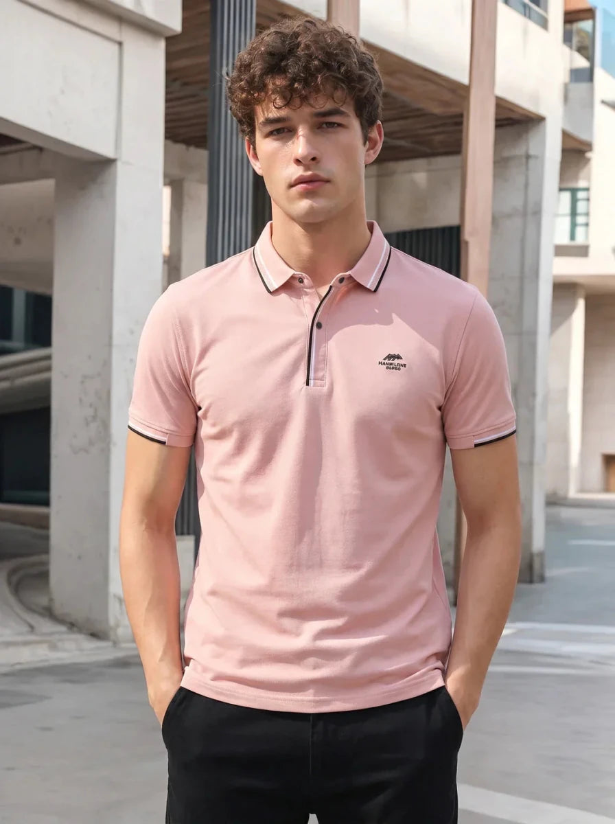 Young man wears 98degreenorth Men's Pink Polo T-Shirt—Handmade Series, standing outdoors in the city.