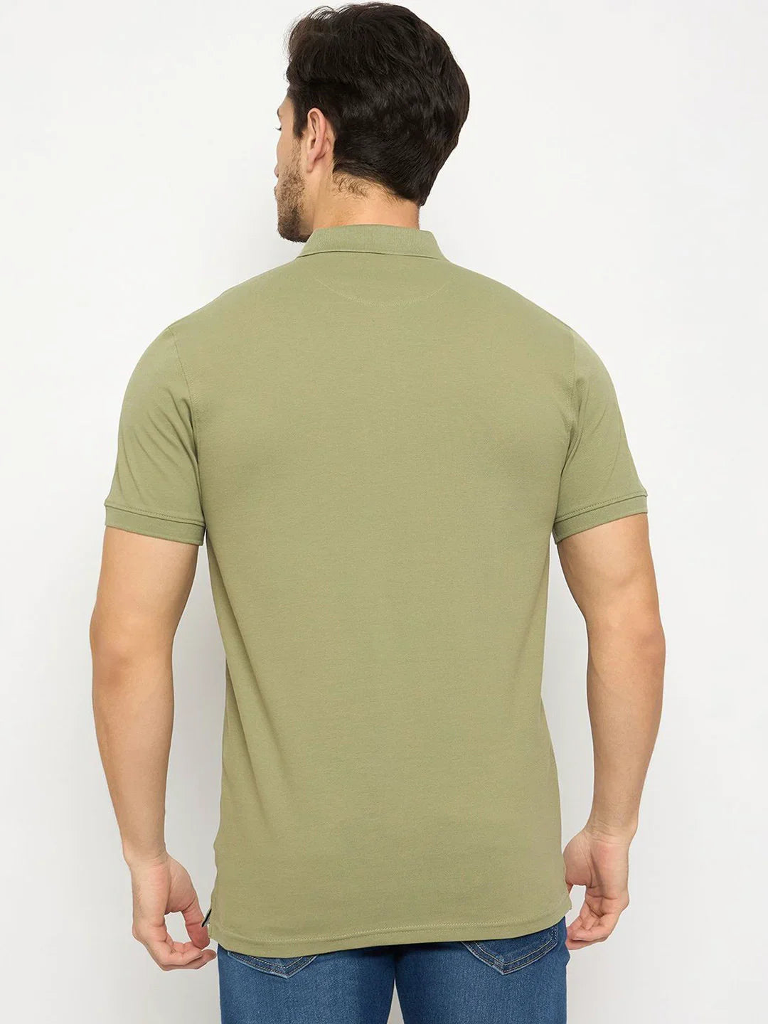 A man in a Men's Pista Green Polo T-Shirt by 98degreenorth and blue jeans, viewed from the back on a white background.