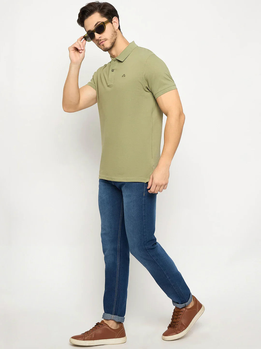 Man in a 98degreenorth Men's Pista Green Polo T-Shirt adjusts sunglasses, paired with blue jeans and brown sneakers.