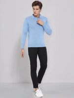 A man wears the 98degreenorth Men’s Sky Blue Merino Wool Polo Sweater with black pants and white sneakers.