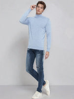 A man wears a 98degreenorth men's sky blue merino wool turtleneck sweater and skinny jeans with white sneakers.