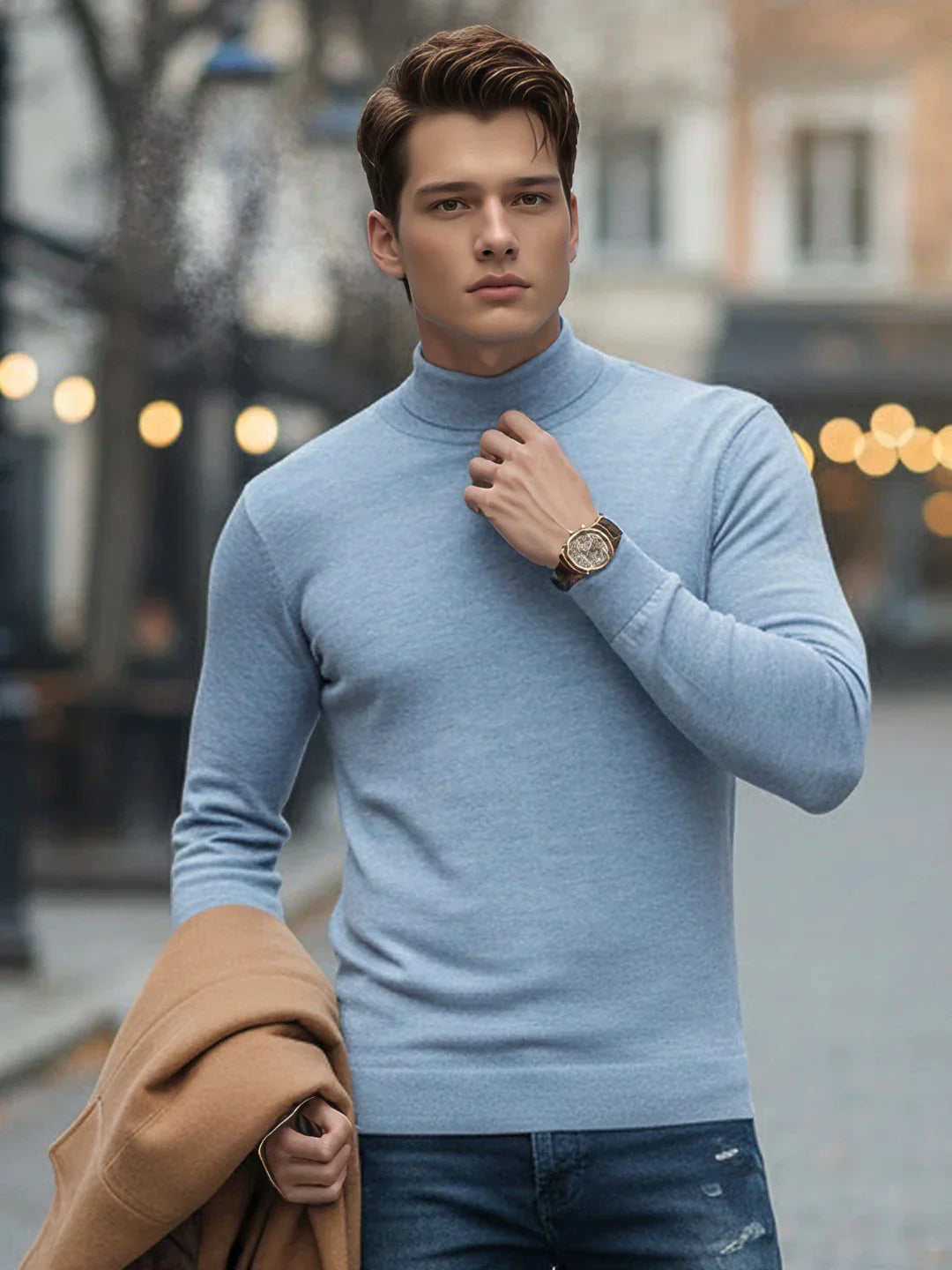 A young man in a 98degreenorth Sky Blue Merino Wool Turtle Neck Sweater and jeans holds a tan coat on a city street.