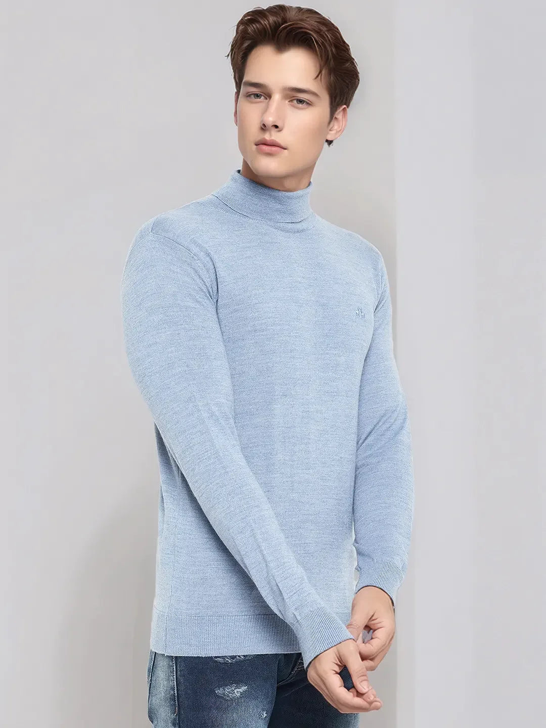 Man in a 98degreenorth Men’s Sky Blue Merino Wool Turtle Neck Sweater and blue jeans on a plain light background.