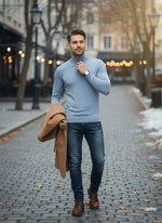 A man in a 98degreenorth Men’s Sky Blue Merino Wool Turtle Neck Sweater and jeans walks on a cobblestone street.