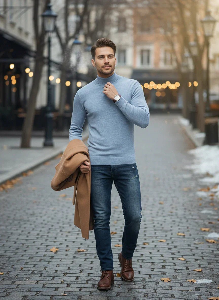 A man in a 98degreenorth Men’s Sky Blue Merino Wool Turtle Neck Sweater and jeans walks on a cobblestone street.