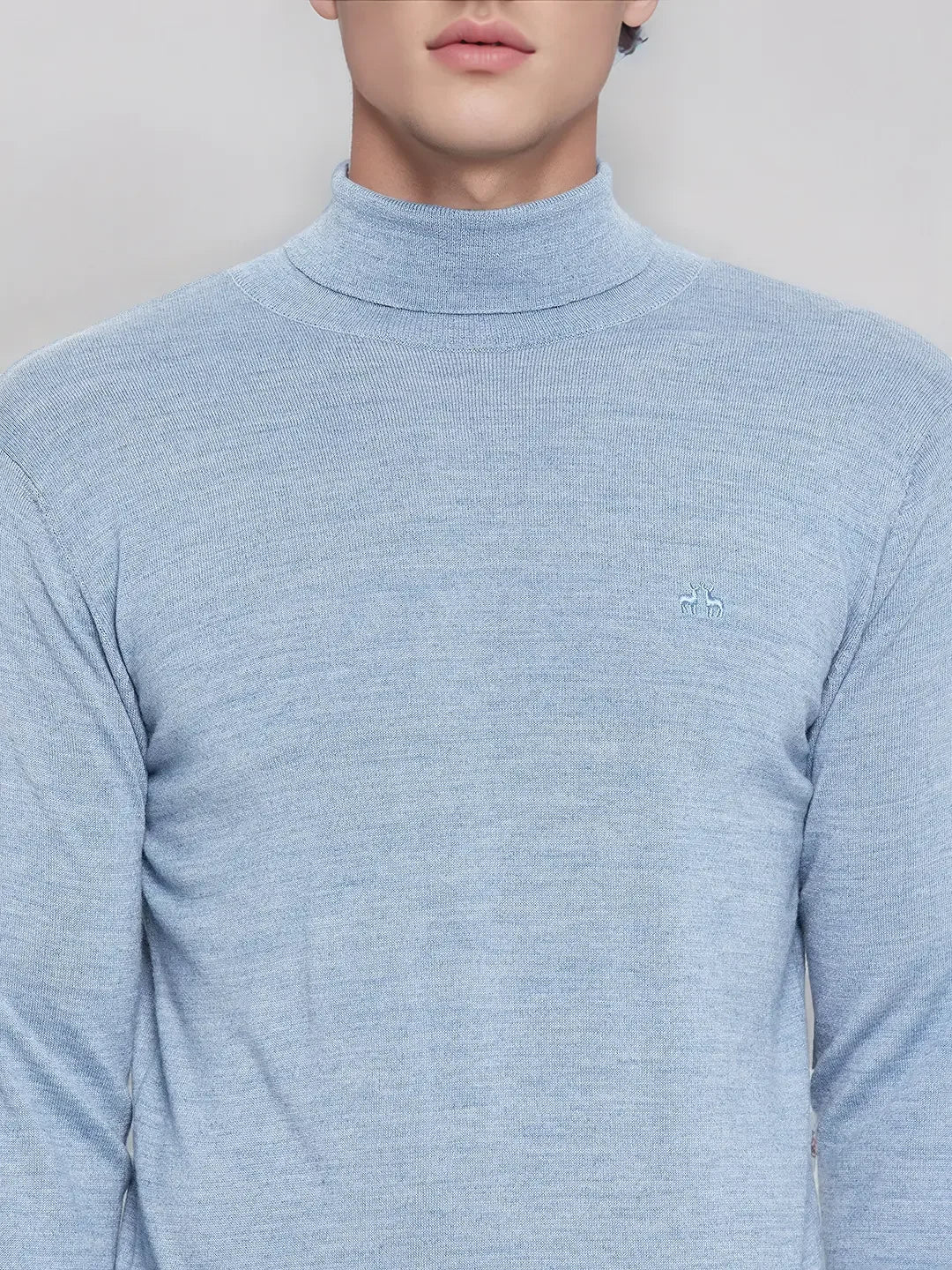 Man in a 98degreenorth men’s sky blue merino wool turtleneck sweater with embroidered logo on the left chest.
