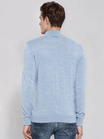 A man in a 98degreenorth sky blue merino wool turtleneck sweater and jeans stands facing away against a plain background.