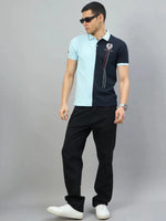 Man in black jeans and a sky blue & navy colour block polo by 98degreenorth stands against a gray background.