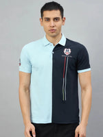 Man in a Men's Sky Blue & Navy Colour Block Polo T-Shirt by 98degreenorth, standing against a plain grey background.