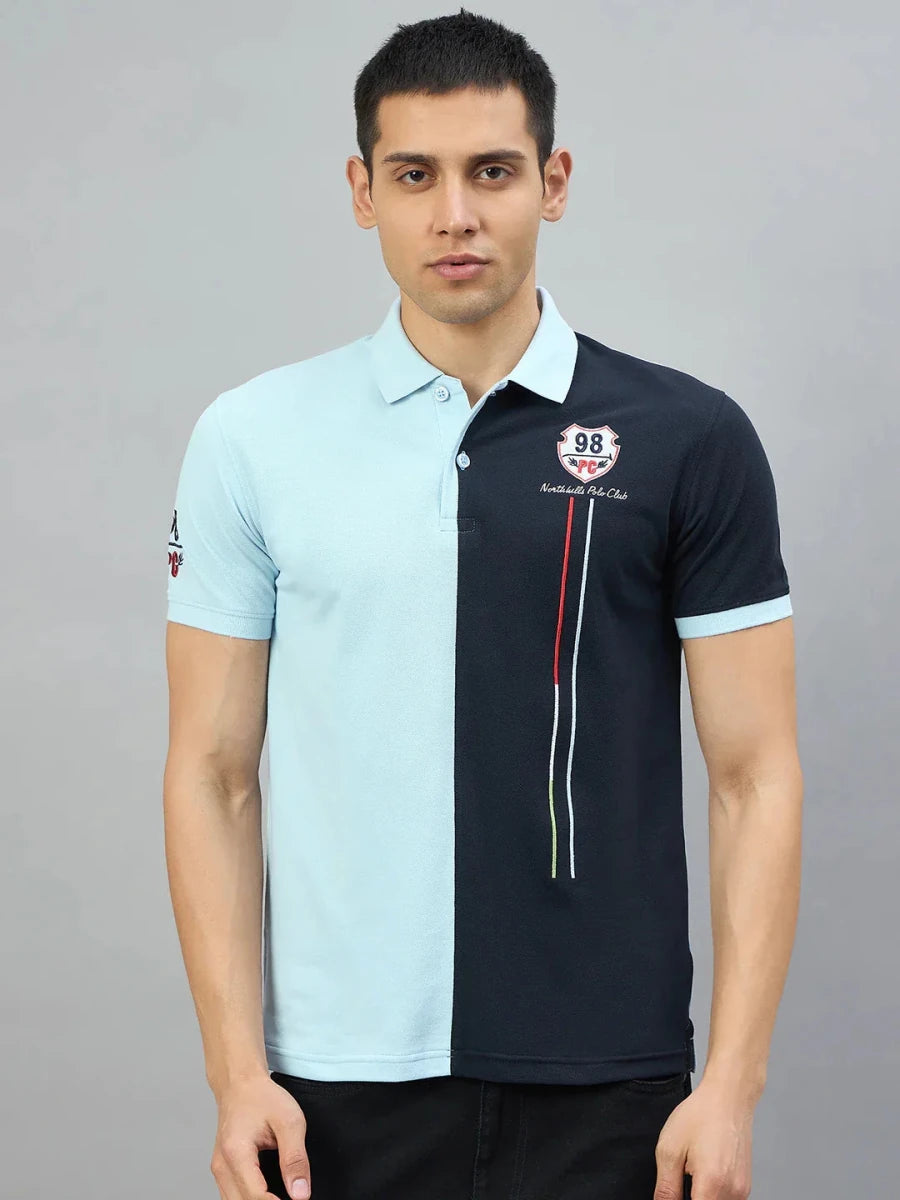 Man in a Men's Sky Blue & Navy Colour Block Polo T-Shirt by 98degreenorth, standing against a plain grey background.